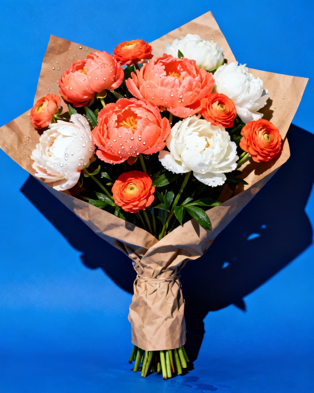 Coral and white peonies wrapped in kraft paper on cobalt blue